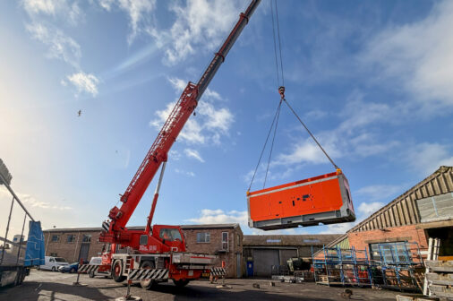 Large industrial pump enclosure being lifted by a crane onto a lorry.